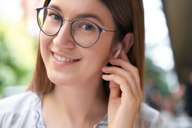 Retrato de primer plano de una mujer caucásica sonriente con anteojos escuchando música sosteniendo auriculares