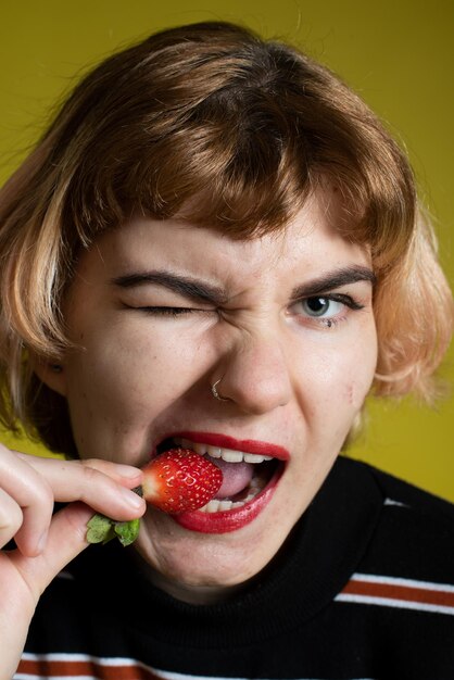 Retrato en primer plano de una mujer comiendo fresa contra un fondo amarillo