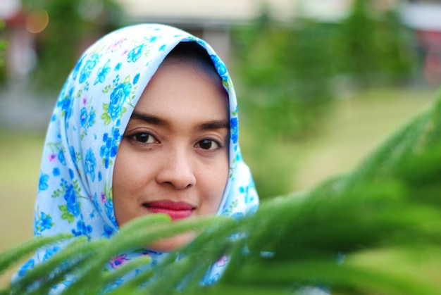 Foto retrato en primer plano de una mujer con hijab junto a plantas en un parque