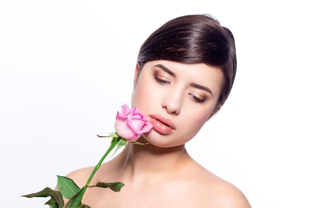 Retrato de primer plano de una mujer joven con maquillaje natural sosteniendo una rosa rosa.