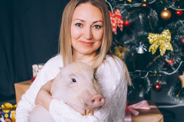 Retrato de primer plano de una mujer joven con un mini cerdo en decoraciones de año nuevo