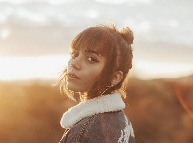 Retrato en primer plano de una mujer joven de pie contra un cielo nublado durante la puesta de sol