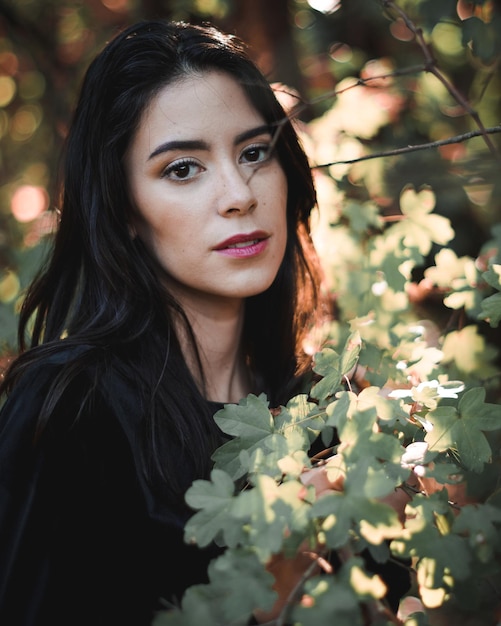 Foto retrato en primer plano de una mujer joven de pie junto a un árbol