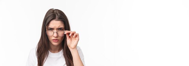 Retrato de primer plano de una mujer joven sospechosa de aspecto serio que mira desde debajo de las gafas entrecerrando los ojos en perso