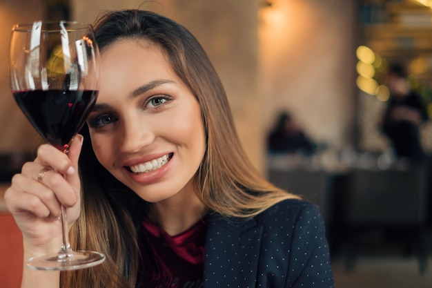 Retrato en primer plano de una mujer joven sosteniendo un vaso de vino en un restaurante