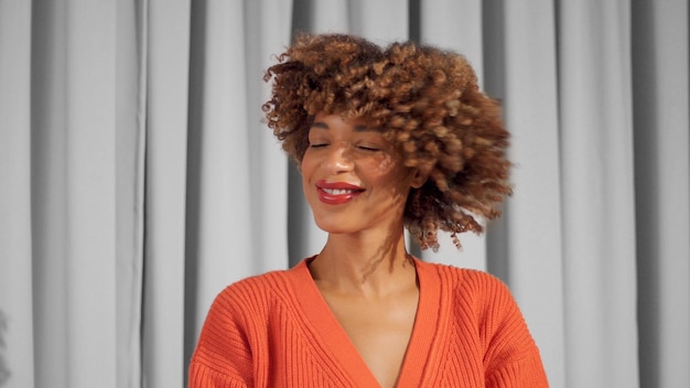 Retrato de primer plano de una mujer negra de raza mixta sonriendo y sacudiendo su cabello Cabello rizado en movimiento