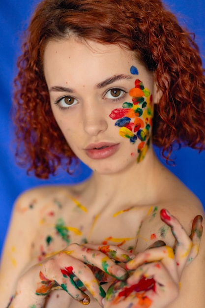 Retrato de primer plano de mujer de pelo rojo rizado Joven alegre manchada de pintura. Retrato de una niña con un patrón creativo en su rostro. Fotografía conceptual para arte o blog de mujeres