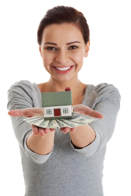 Foto retrato en primer plano de una mujer sonriente sosteniendo una casa modelo y dinero de papel contra un fondo blanco