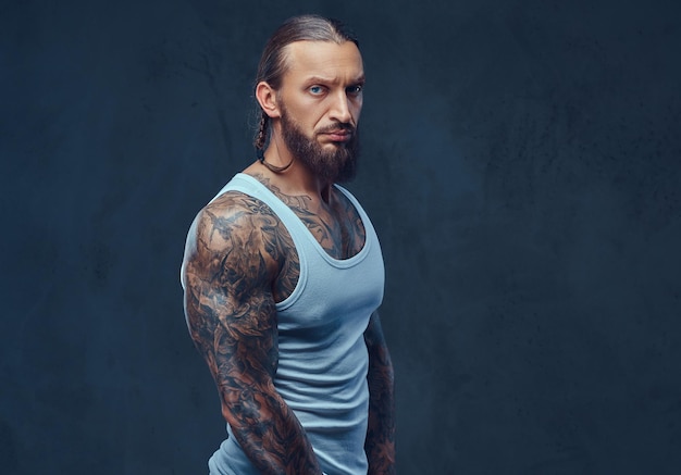 Retrato de primer plano de un musculoso hombre tatuado barbudo desnudo con un elegante corte de pelo en ropa deportiva. Aislado en un fondo oscuro.