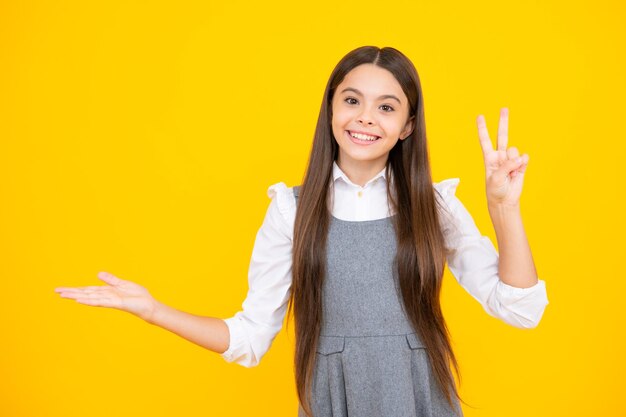 Retrato en primer plano de una niña adolescente que se muestra en el espacio de copia apuntando a anuncios publicitarios aislados sobre un fondo amarillo