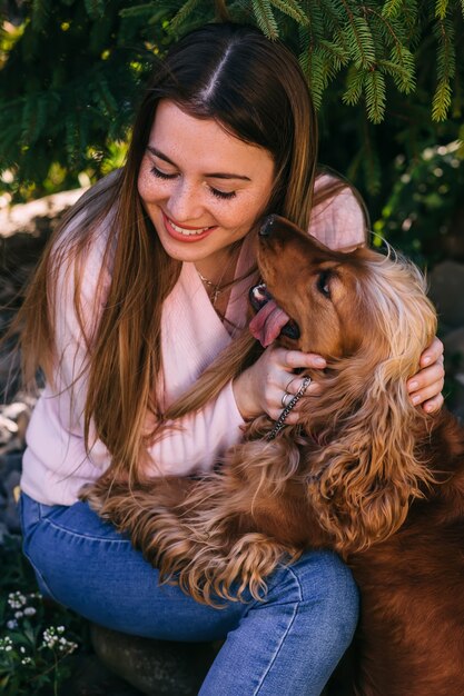 Retrato de primer plano de niña complacida con perro abrazando de pelo largo con los ojos cerrados. Mujer joven sonriente disfrutando de un buen día y posando con la mascota en el patio