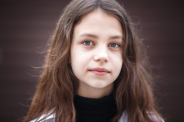 Retrato de primer plano de una niña hermosa y elegante con el pelo largo que fluye contra una pared de rayas marrones