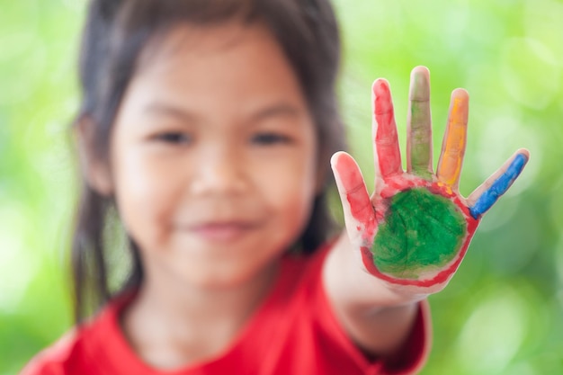 Foto retrato en primer plano de una niña que muestra pintura de colores en la mano
