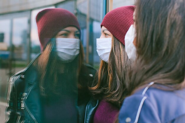 Retrato de primer plano de niñas con máscaras médicas. En el contexto de un edificio de cristal con reflejos. Concepto sobre el tema de viros.