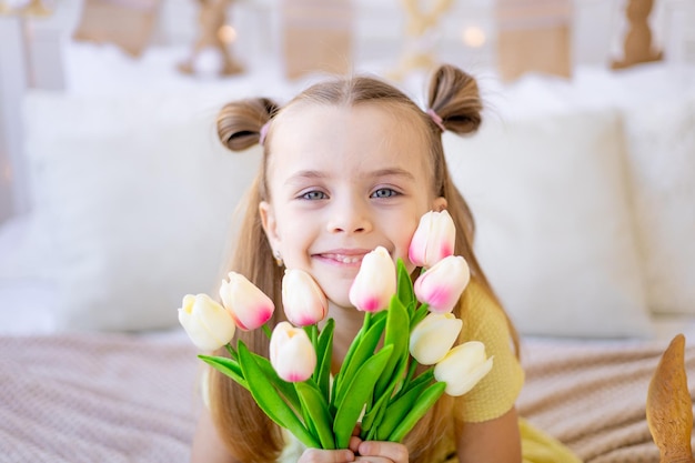 Retrato de primer plano de un niño lindo con flores de primavera tulipanes rosas sonriendo y regocijándose o dando como regalo el día de la mujer o el día de la madre