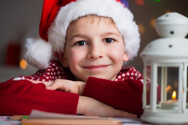 Retrato en primer plano de un niño lindo con sombrero de Papá Noel sentado junto a una lámpara de aceite en casa