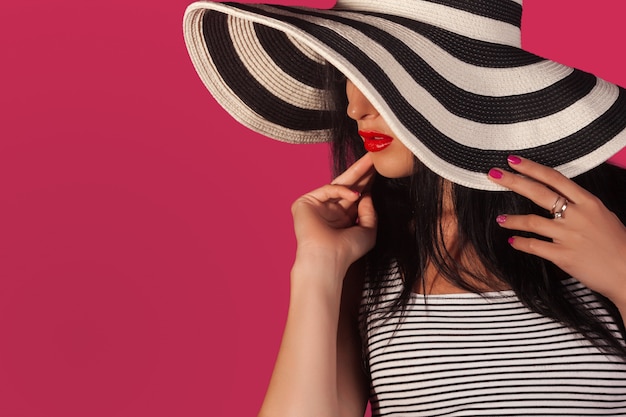 Retrato de primer plano o atractiva mujer con sombrero protector solar despojado. Mujer hermosa irreconocible en pared rosa