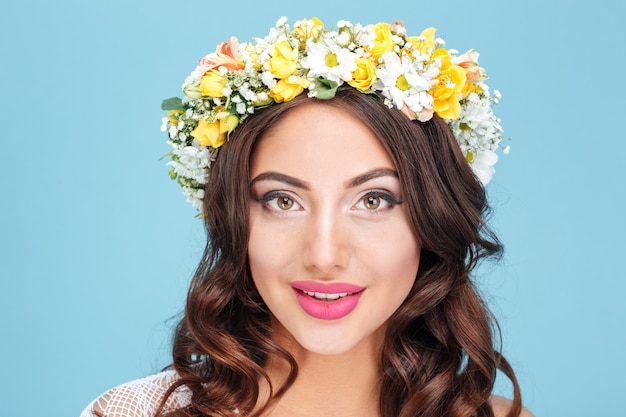 Retrato de primer plano de una sexy morena con diadema de flores aislada sobre fondo azul