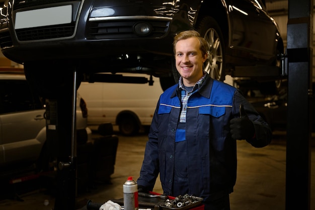 Retrato profesional de un apuesto hombre caucásico, mecánico de automóviles, técnico, ingeniero de automóviles, sonriendo a la cámara de pie cerca de una caja con herramientas para reparar automóviles en el taller de reparación