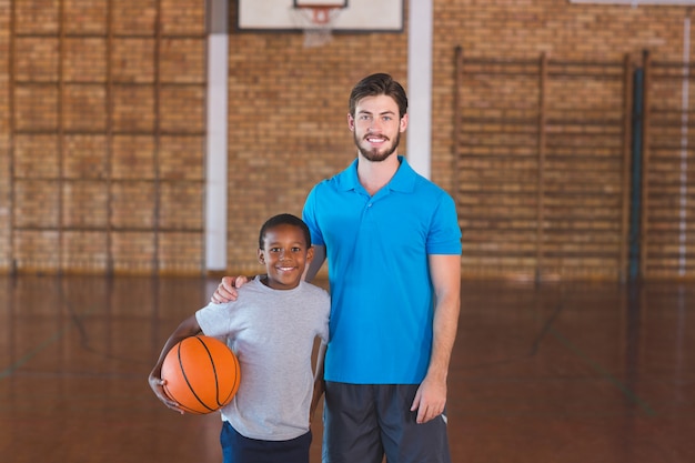 Retrato del profesor de deportes de pie con su alumno en la cancha de baloncesto