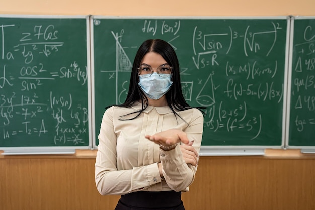 Retrato de profesor con máscara médica durante la epidemia de coronavirus de pie contra la pizarra. Lección de matemáticas educativas