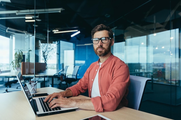 Retrato de un programador exitoso dentro de la oficina, un hombre con gafas de barba y una camisa roja