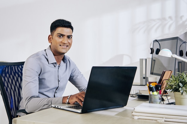 Retrato del programador indio sonriente trabajando con un portátil en la oficina