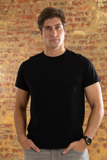 Foto retrato próximo de um jovem caucasiano vestindo uma camiseta preta em pé contra uma parede de tijolos, olhando para a câmera