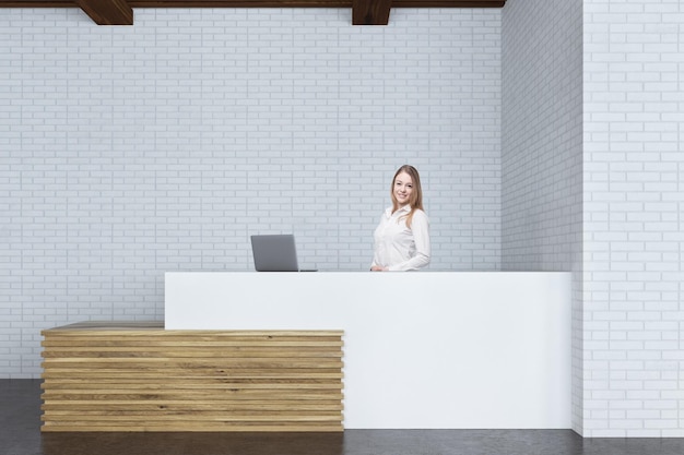 Retrato de una recepcionista rubia parada en un mostrador blanco y de madera con una computadora portátil gris. representación 3d