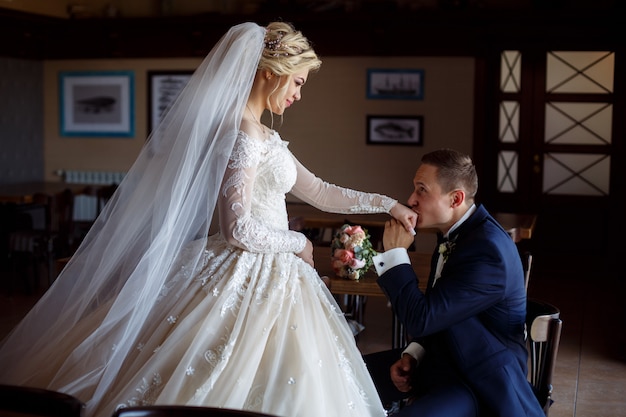 Retrato de recién casados felices. El novio besa la mano de la novia en el interior con estilo en el interior. Las novias se miran suavemente. día de la boda. momento romantico