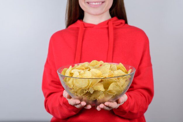 Retrato recortado da foto do close up de positivo alegre legal com fome em um adolescente de pulôver vermelho brilhante segurando uma tigela grande nas mãos isoladas de fundo cinza