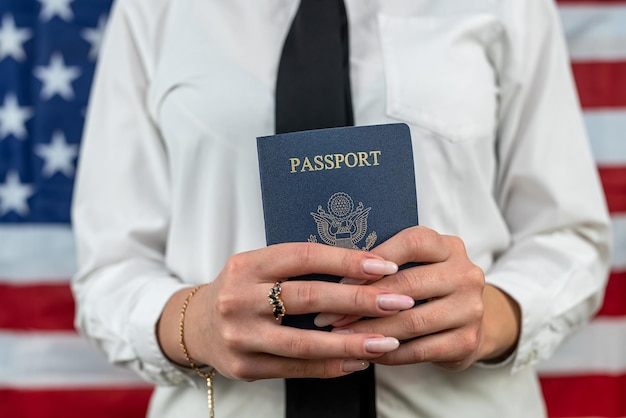 Retrato recortado de um jovem comissário de bordo segurando um leque de dólares e um passaporte americano e de pé contra um controle de passaporte de viagem de fundo de bandeira americana