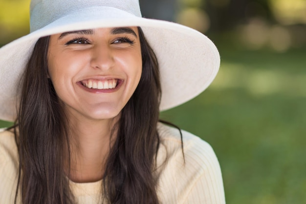 Retrato recortado de uma jovem caucasiana sorridente e feliz usando um chapéu branco ao ar livre no parque Estilo de vida e humor de celebração