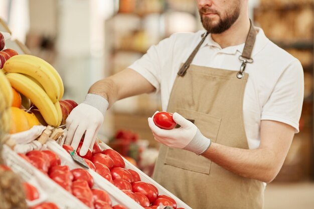 Retrato recortado de hombre barbudo sosteniendo tomates orgánicos frescos mientras vende productos locales en el puesto de frutas y verduras en el mercado de agricultores