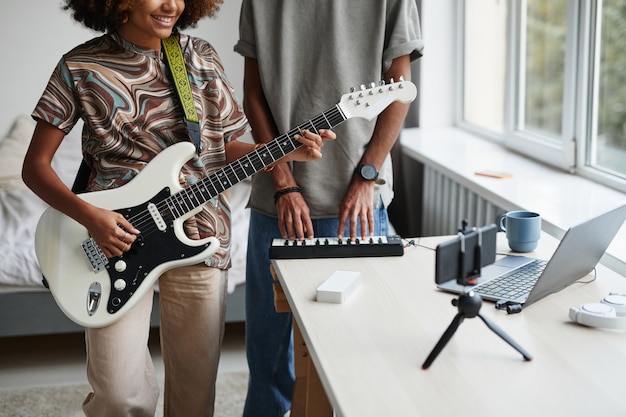 Retrato recortado de joven afroamericana tocando la guitarra en casa y grabando video o transmisión en vivo, espacio de copia