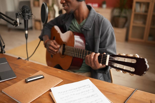 Retrato recortado del talentoso afroamericano cantando al micrófono y tocando la guitarra mientras graba música en el estudio, espacio de copia