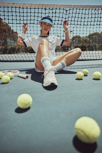 Retrato de relajación y mujer de tenis en la red para hacer ejercicio físico y descanso en la cancha en el campo de deportes Entrenamiento de entrenamiento y cardio de la chica del club de atletas profesionales descansando en el piso con pelotas de tenis