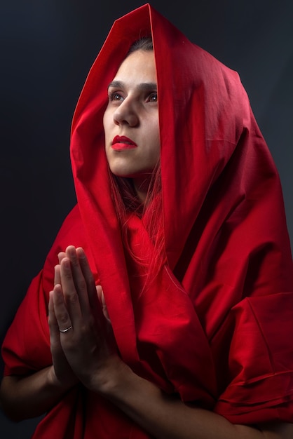 Retrato religioso dramático menina de vermelho reza com as mãos postas.