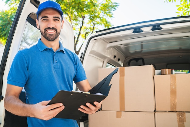 Foto retrato de un repartidor comprobando los productos en la lista mientras está de pie junto a su camioneta. concepto de entrega y envío.