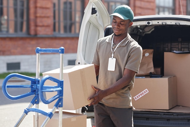 Retrato de un repartidor sonriente descargando cajas al aire libre en el espacio de copia de la luz del sol