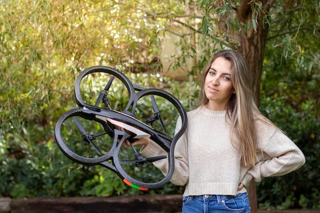 Retrato retroiluminado de una chica caucásica mostrando a la cámara su nuevo dron cuadricóptero de iniciación en la naturaleza