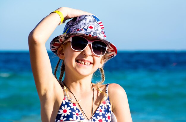 Retrato de una risa adolescente de piel clara con gafas de sol y un sombrero con el telón de fondo del mar