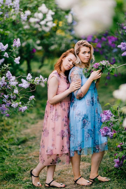 Retrato romântico de irmãs gêmeas em vestidos concursos posando no parque de verão.