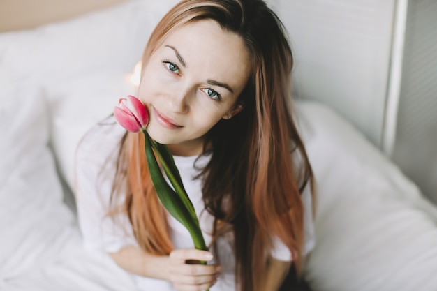 Retrato romântico de uma bela jovem feliz na cama com tulipas cor de rosa frescas