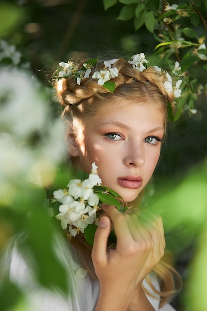 Retrato romântico de uma garota no parque perto de uma macieira em flor. cosméticos naturais. beleza natural de uma mulher em um vestido branco