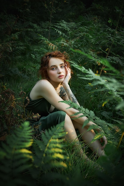 Retrato romántico de una mujer en un helecho en el bosque. Maquillaje natural de mujer de arte descansando en la naturaleza. Matorrales de helechos verdes