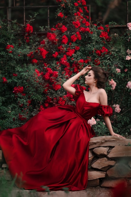 Retrato romántico de una mujer hermosa vestida de rojo en el jardín lleno de rosas