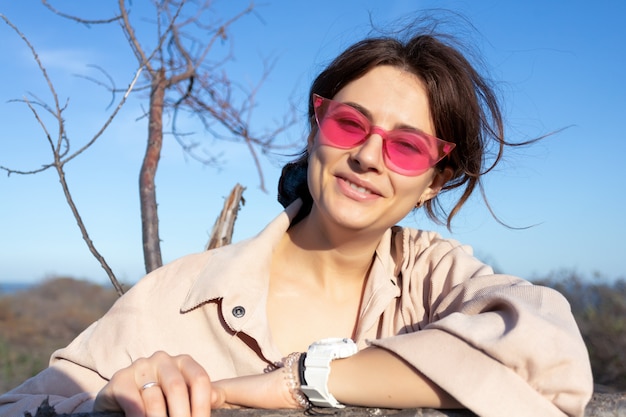 Retrato romántico de una mujer joven con el pelo rizado en gafas retro jeans contra árbol, bosque. Retrato creativo mujer en la naturaleza. Concepto de arte de diseño