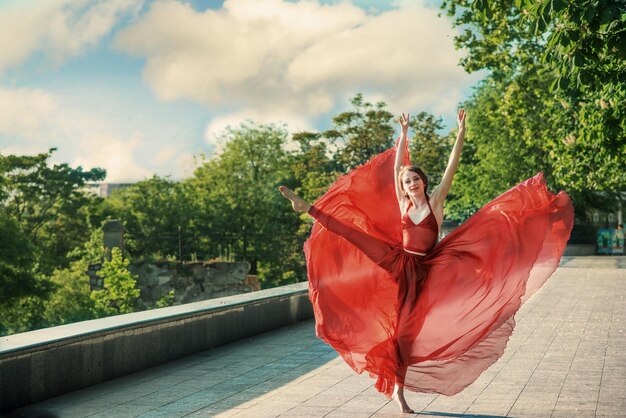 Retrato romántico de la mujer en vestido rojo aireado bailando en el bulevar