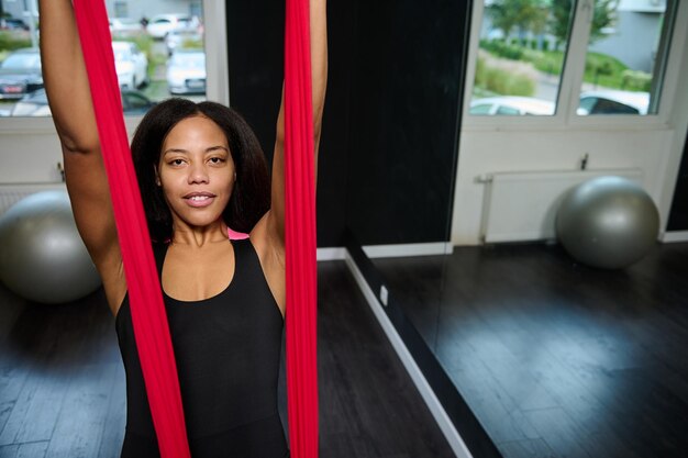 Retrato de rostro de una joven mujer africana de cuerpo delgado deportivo con correas en clase de yoga aérea voladora con hamaca roja